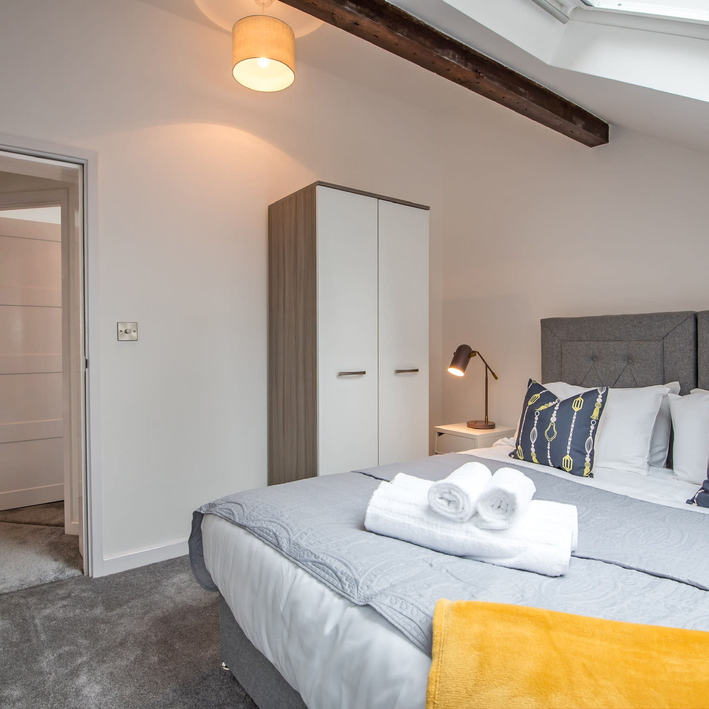 A modern bedroom with a bed, a wardrobe, a bedside table with a lamp, and a headboard.