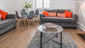 A modern living room with a grey sofa, a round glass coffee table, and a dining area with a glass table and chairs. - The Kirkham (Durham)