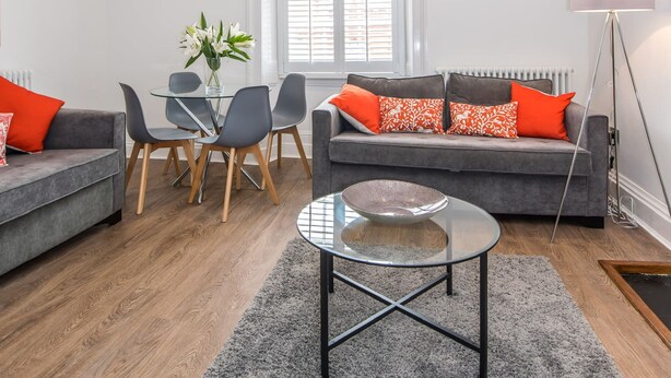 Ein modernes Wohnzimmer mit einem grauen Sofa, einem runden Glastisch und einem Essbereich mit einem Glastisch und Stühlen.