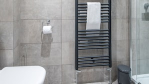 Ein modernes Badezimmer mit einer Duschkabine aus Glas, einem schwarzen Handtuchhalter mit einem weißen Handtuch und einem Toilettenpapierhalter an der Wand.
