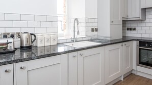 Eine moderne Küche mit weißen Schränken, einer Granit-Arbeitsplatte, einem Edelstahl-Wasserkocher, einem Toaster und einem Einbauofen.