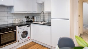 A modern kitchen with white cabinets, a built-in oven, a washing machine, and a sink. - The Tunstall (Durham)