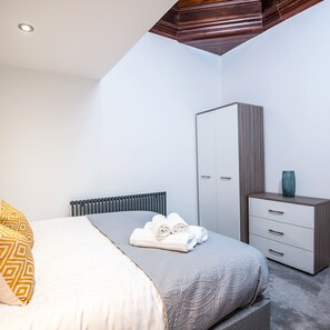 A bedroom with a bed, a wardrobe, and a small table with towels. - The Tunstall (Durham)