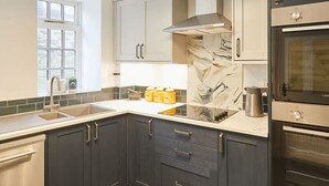 A modern kitchen with dark cabinets, a stainless steel range hood, a double oven, and a window providing natural light. - Host Stay Dotty s Coastal Retreat (Saltburn-by-the-Sea)