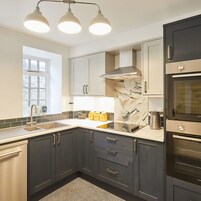 A modern kitchen with dark cabinets, a stainless steel range hood, a double oven, and a window providing natural light.