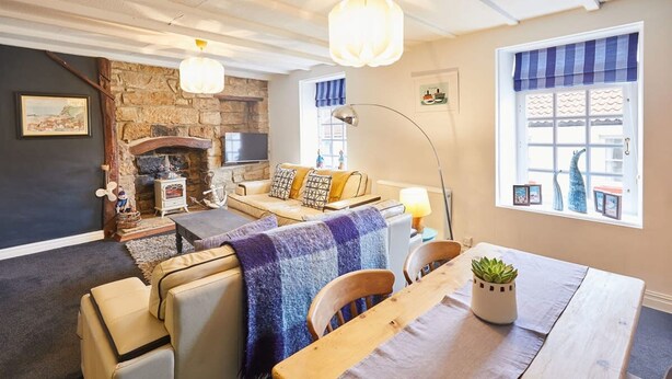 A cozy living room with a stone fireplace, a sofa, a dining table, and a large window with a view. - Host Stay Dotty s Coastal Retreat (Saltburn-by-the-Sea)