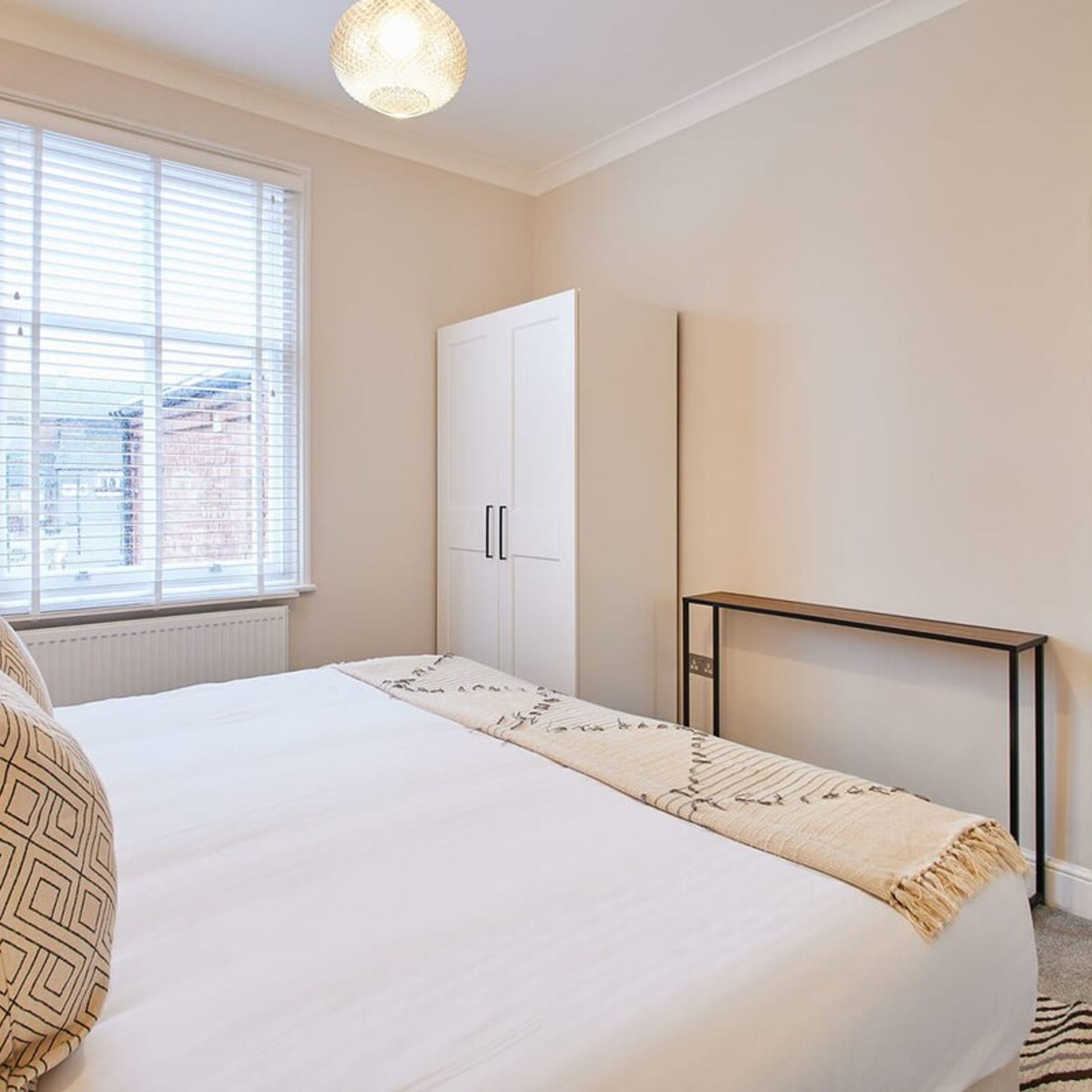 Ein Schlafzimmer mit Bett, Kleiderschrank, Nachttisch und einem Fenster mit Jalousien.