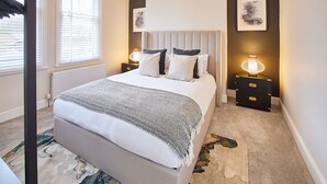 A bedroom with a large bed, two bedside tables, a radiator, and a window with blinds. - Host Stay Belle Vue (Saltburn-by-the-Sea)