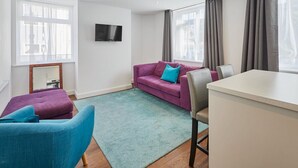A modern living room with a purple sofa, a blue armchair, a small table, and a TV mounted on the wall. - Host Stay The Globe Apartment 3 (Guisborough)