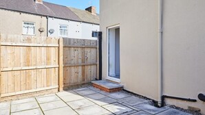 A paved backyard with a wooden fence, a door, and a white wall with a gutter. - Host Stay The Globe Apartment 3 (Guisborough)
