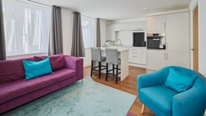 A modern living room with a purple sofa and a blue armchair, a small kitchen area with white cabinets, and a dining table with chairs. - Host Stay The Globe Apartment 3 (Guisborough)