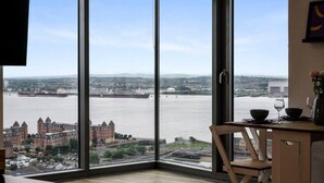 A room with large windows offering a view of a river and buildings. - Host Apartments Kings Dock View Baltic Living (Liverpool)