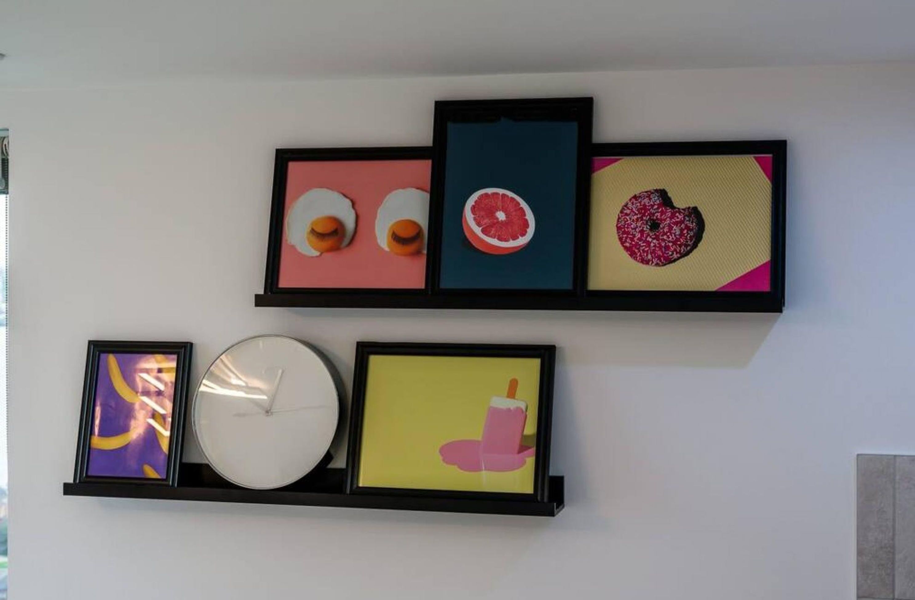 Una pared con cinco obras de arte enmarcadas y un reloj.