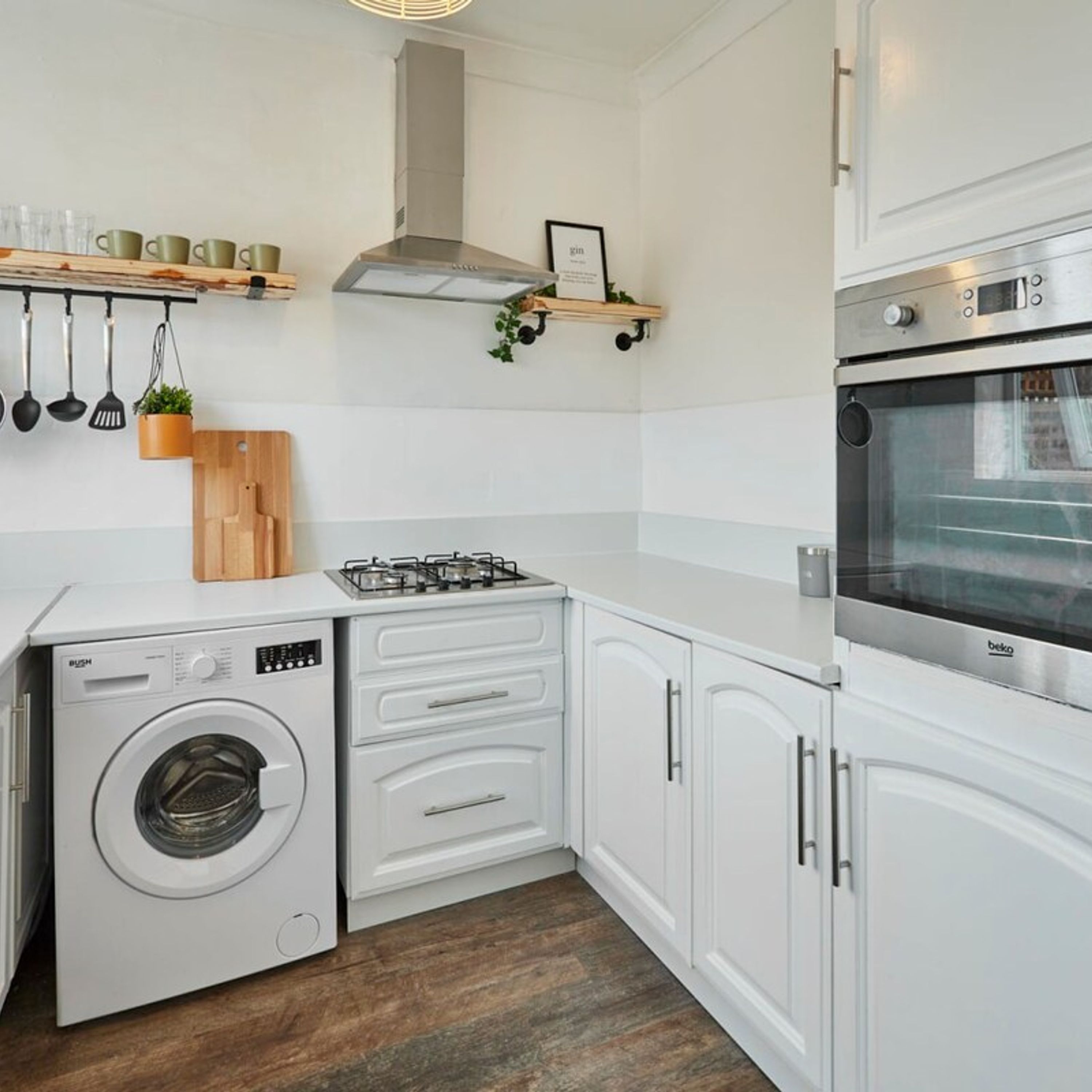 A compact kitchen with white cabinetry, a built-in washing machine, a gas stove, and a stainless steel oven.