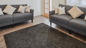 A modern living room with two grey sofas, a dark grey rug, and a wooden door. - Host Stay Church Street (Warrington)