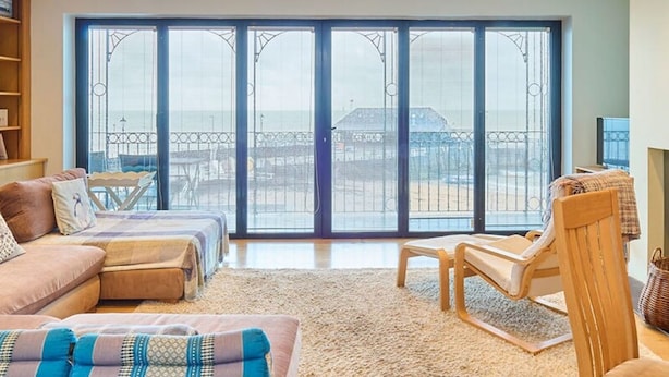 Ein geräumiges Wohnzimmer mit einem großen Schiebeglastür, die auf einen Balkon führt, einer Sofagarnitur, einem Holzstuhl und einem Teppich.