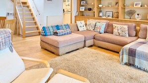 Ein modernes Wohnzimmer mit einer Eckcouch, einer Holztreppe und eingebauten Regalen mit Dekoration.