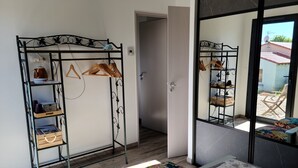 Une pièce avec une armoire en métal, un lit recouvert d’une couvre-lit à motifs et une vue sur l’extérieur par une porte vitrée.