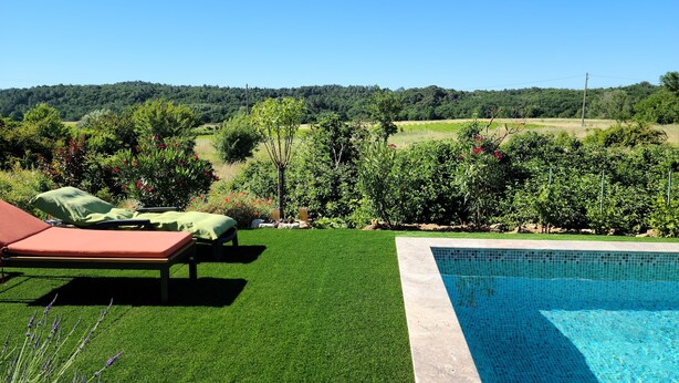 Un espace piscine offrant une vue dégagée sur une pelouse verdoyante, avec un fauteuil de relaxation et une vue sur un paysage lointain.