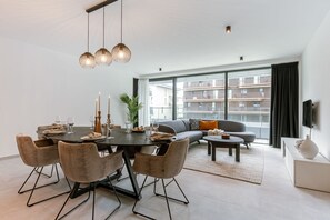 A modern living room with a dining area, large windows, and a view of a building. - BE OST Vict 7-0204 in Oostende (Ostend)