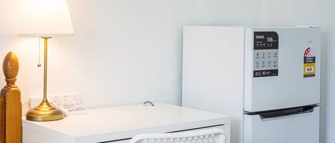 A white desk with a lamp, a white chair, and a white refrigerator with a digital control panel.