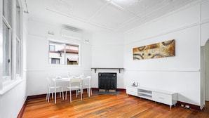 A room with a fireplace, a dining table with chairs, a white TV stand, and a large abstract painting on the wall. - Metawise/parramatta Cozy Room With Furniture Wifi (Parramatta)