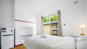 A hotel room with a bed, a desk, a chair, a refrigerator, and a window with a view of greenery. - Metawise/parramatta Cozy Room With Furniture Wifi (Parramatta)