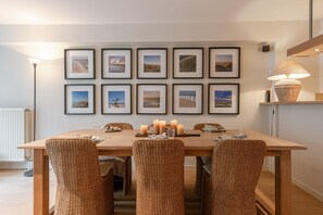Uma sala de jantar com mesa de madeira, cadeiras de vime e quadros nas paredes.