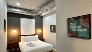 Un dormitorio con una cama, lámparas de noche, una pizarra y una cita enmarcada en la pared.