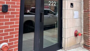 Entrada de un edificio con puerta de cristal, un hidrante y un muro de ladrillo.