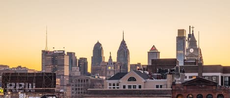 A city skyline at sunset with prominent buildings, including a clock tower and a building with a cross on top.