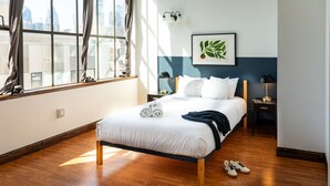 Camera d'albergo ordinata con un letto, un comodino, una lampada e vista sulla città attraverso ampie finestre.