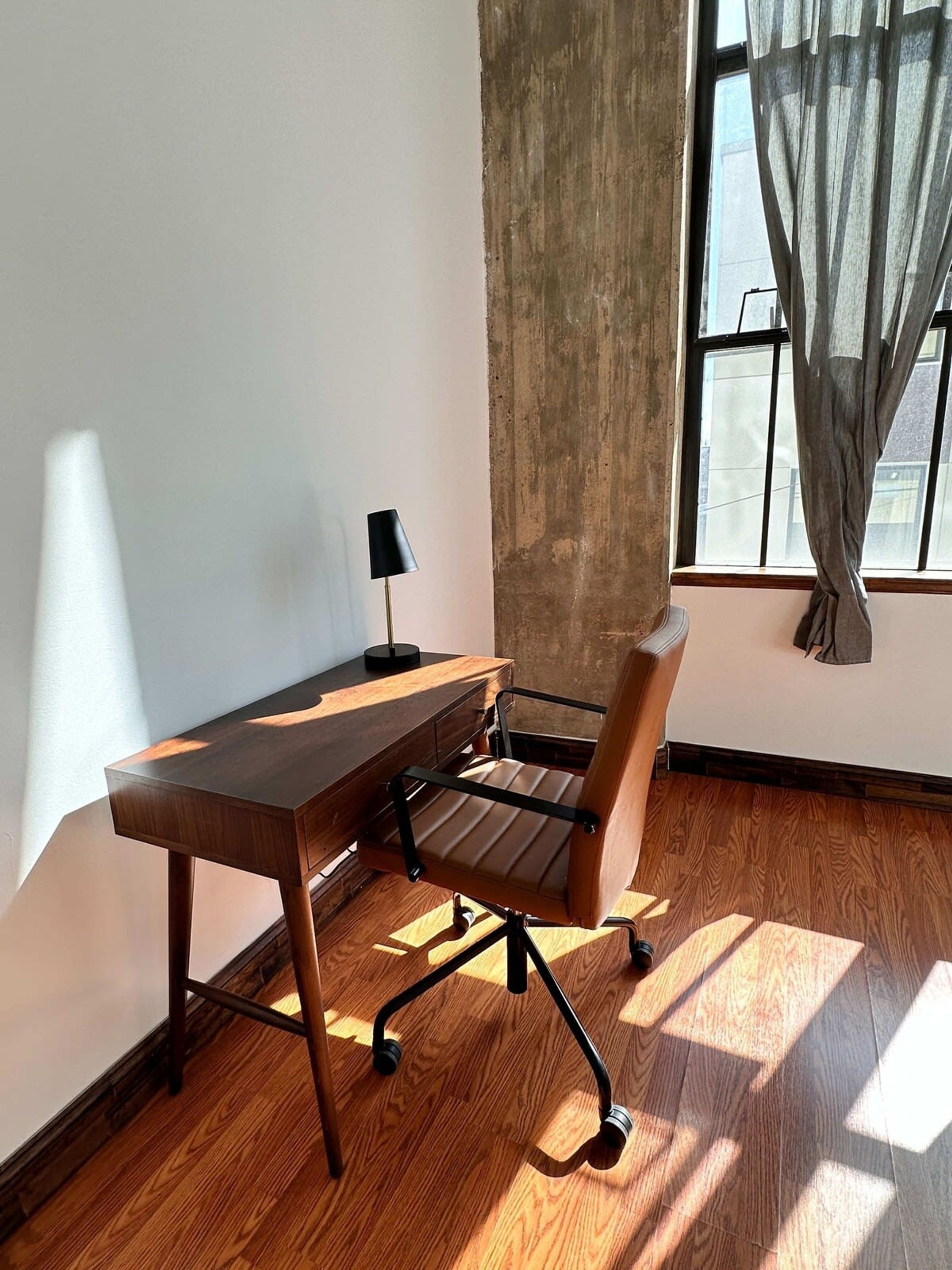 Um espaço de escritório moderno com uma mesa de madeira, uma cadeira de escritório preta e um abajur.