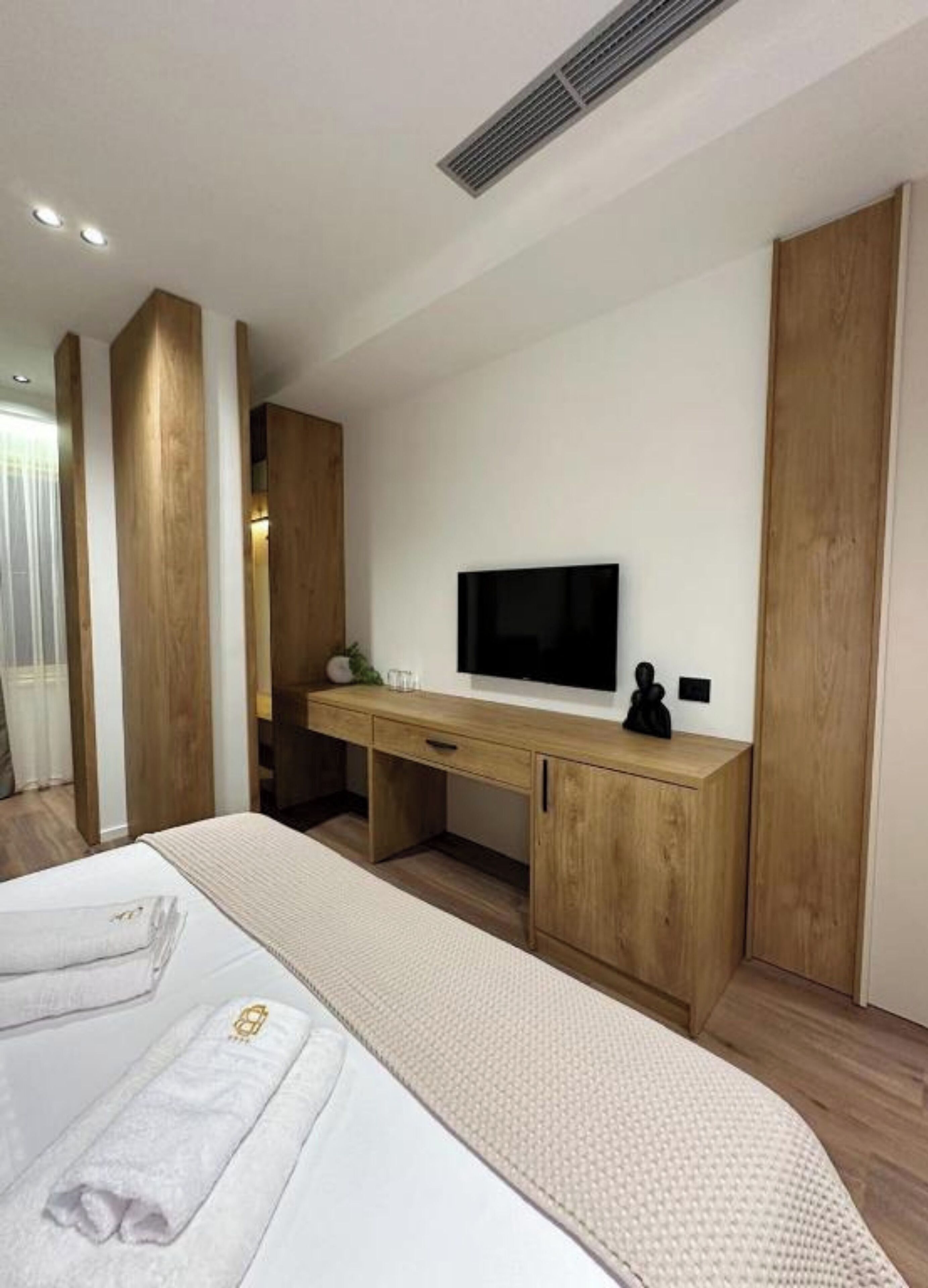 A modern bedroom with a bed, a wooden desk, a flat-screen TV, and a large mirror.