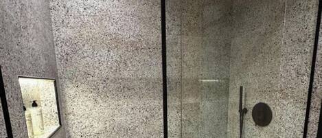 A glass-enclosed shower with a handheld showerhead, a control panel, and a tiled floor.
