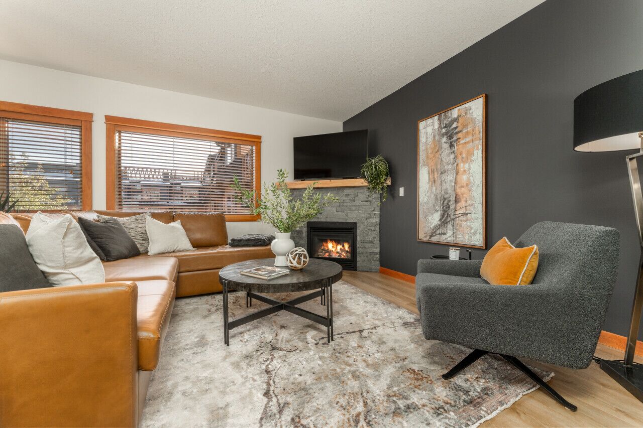 Un salon moderne avec un canapé d’angle, un fauteuil gris, une cheminée et un grand tableau abstrait.