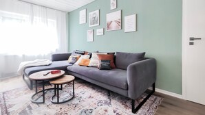 A modern living room with a grey sofa, a patterned rug, and several wall art pieces. - Garden View 1 - Design-Apartment, Küche, Garten - Sauerlanda (Schalksmühle)