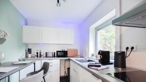A modern kitchen with white cabinets, a black microwave, a coffee maker, and a window providing natural light. - Garden View 1 - Design-Apartment, Küche, Garten - Sauerlanda (Schalksmühle)