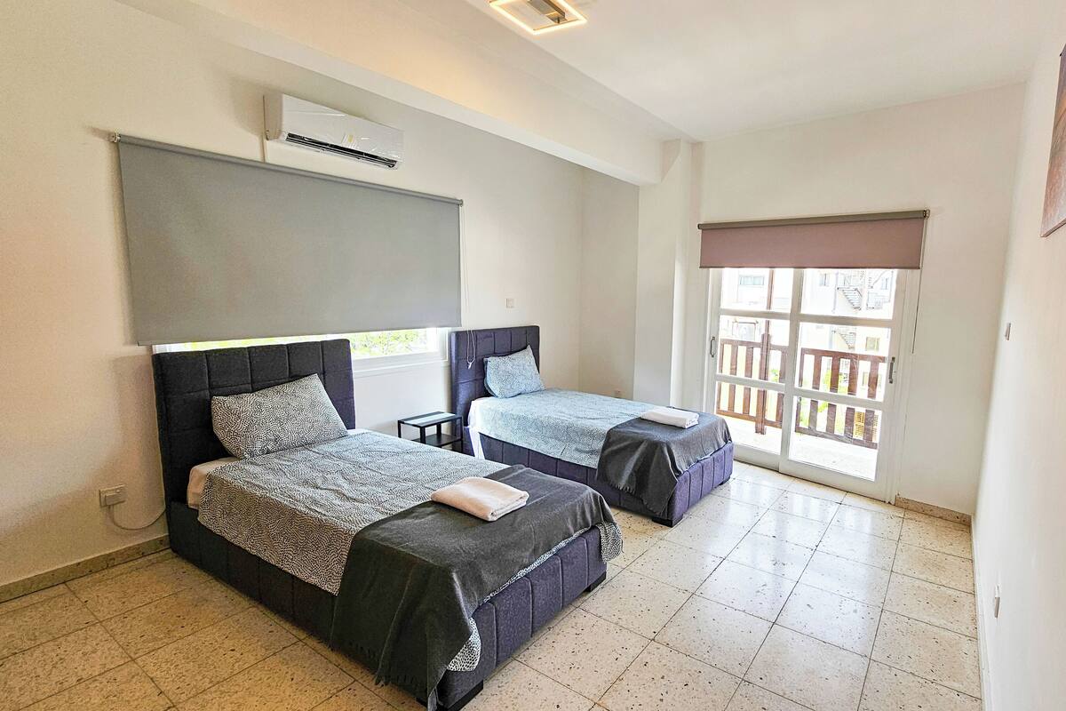 A bedroom with two beds, a window with a view, and an air conditioning unit.