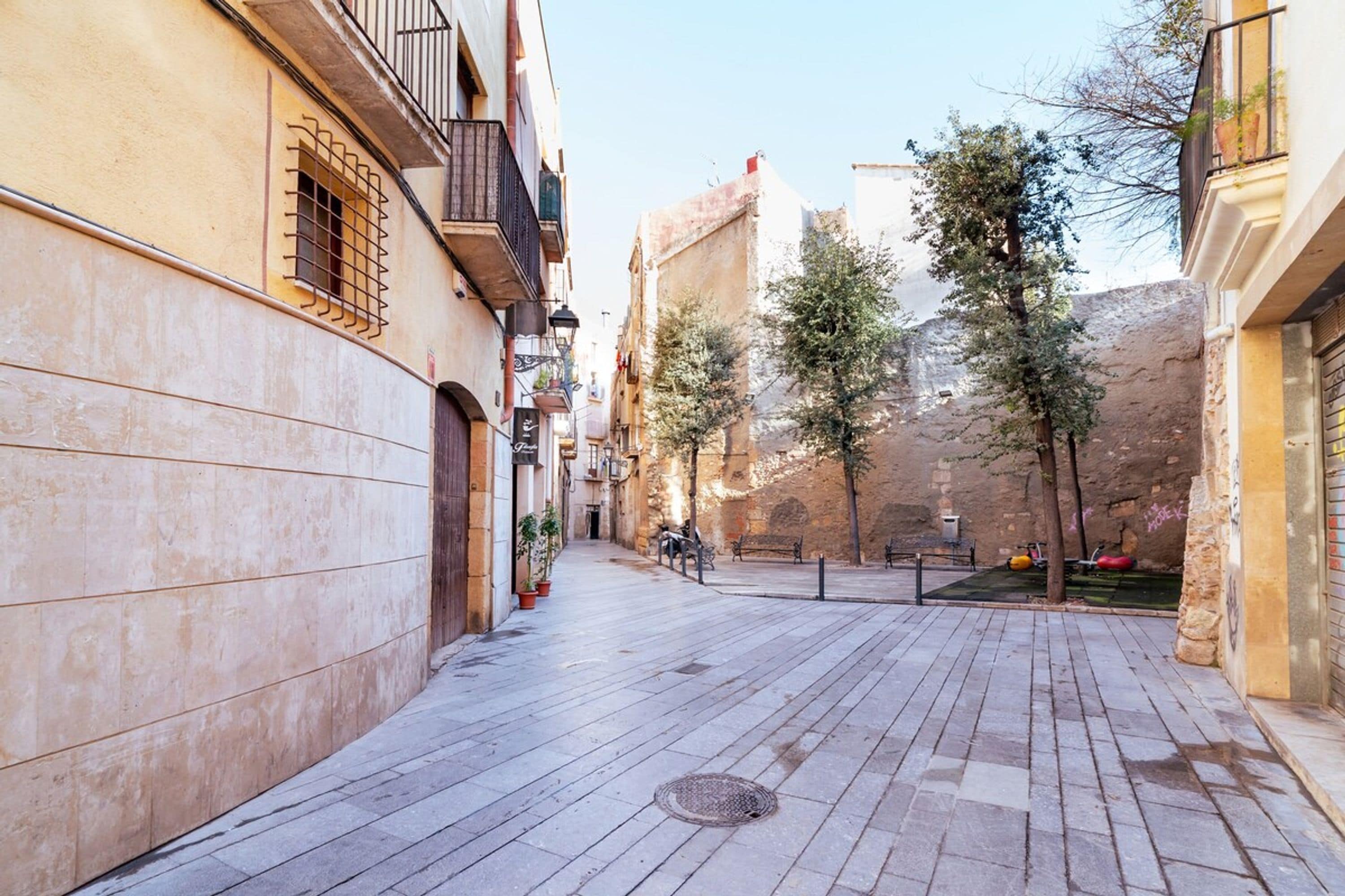Una estrecha calle urbana flanqueada por edificios, un camino pavimentado y algunos árboles.