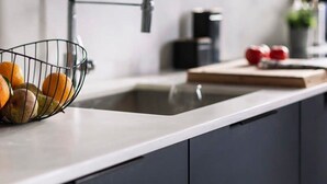 Une cuisine dotée d’un évier moderne, d’un panier de fruits et d’une planche à découper avec des pommes.