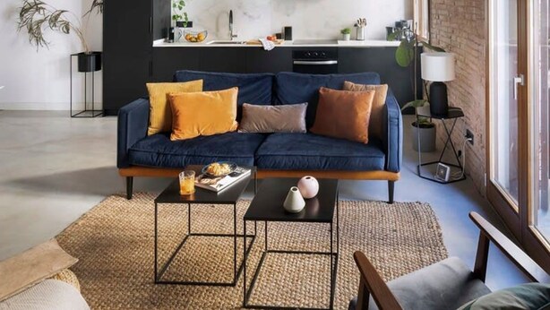 Un salon moderne avec un canapé bleu, une table basse et une cuisine en arrière-plan.