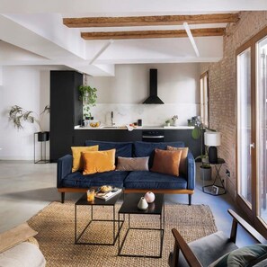 A modern living room with a blue sofa, a coffee table, and a kitchen in the background. - Blue Velvet Premium 2BR Near Plaza Catalunya (Barcelona)