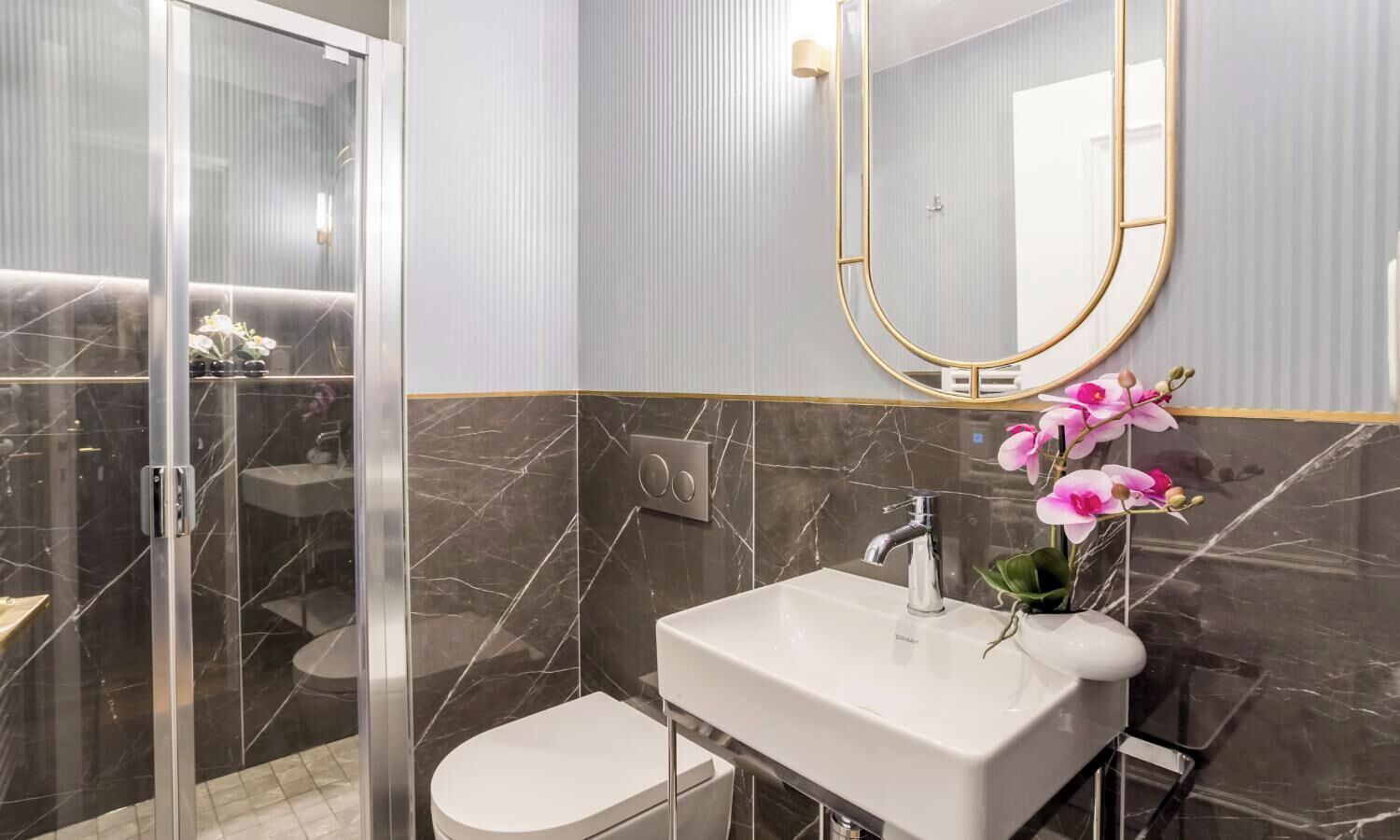 A modern bathroom with a glass-enclosed shower, a white sink with a gold faucet, and a mirror with a gold frame.