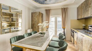 A dining area with a marble table, green upholstered chairs, a large mirror, and a view of the outdoors through a window.