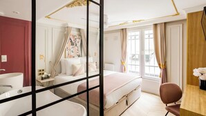 A hotel room with a large bed, a desk, a chair, a bathroom with a sink and bathtub, and a window with curtains.