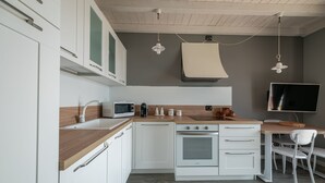 A modern kitchen with white cabinets, a wooden countertop, a built-in oven, a microwave, and a dining area with a table and chairs.
