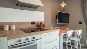 A modern kitchen with a wooden countertop, white cabinets, a built-in oven, and a wall-mounted TV.