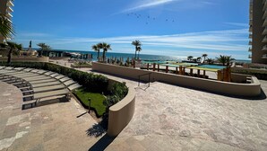 A resort pool area with a clear view of the ocean, palm trees, and a multi-level building. - New 3BR Ground Floor Las Palomas Condo (Puerto Peñasco)