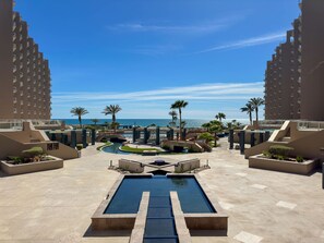 Ein Poolbereich eines Resorts mit einem zentralen Pool, Palmen und Blick auf den Ozean.